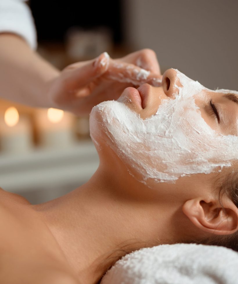 Young beautiful brunette girl in mask for face relaxing in spa salon. Eyes closed. Copy space.